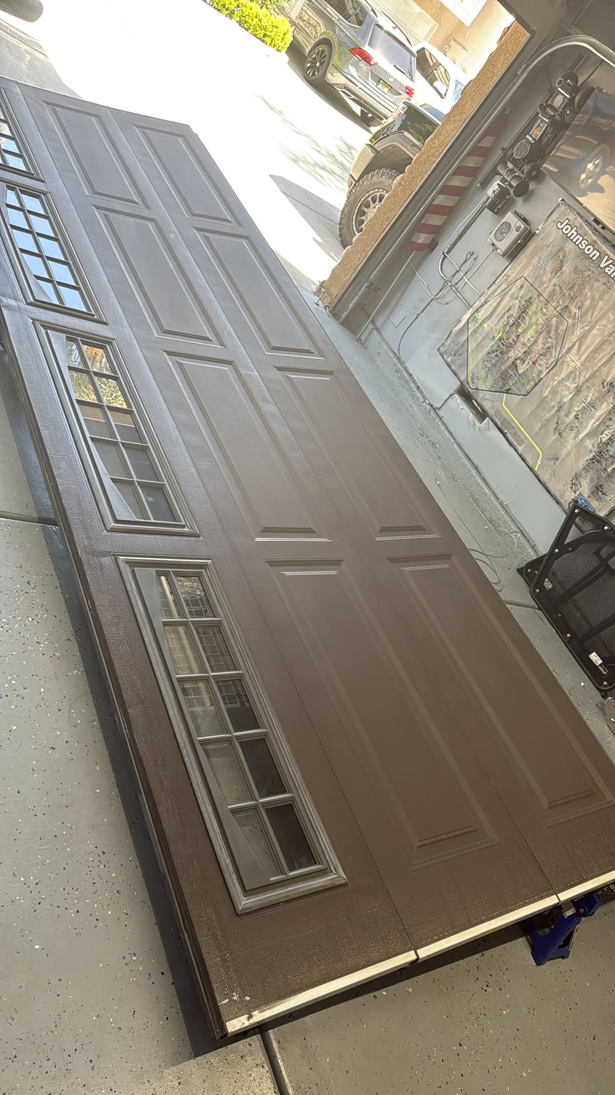 Old brown raised-panel garage door removed and laid out on the driveway