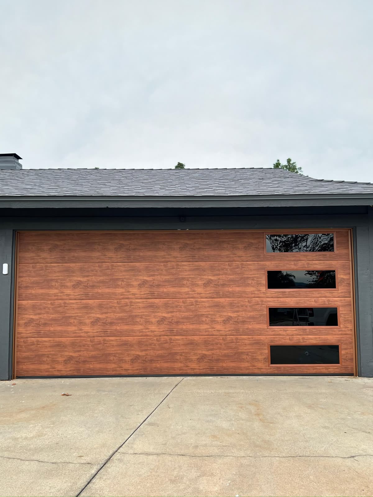 Wood-look modern flush garage door with side windows on a dark gray home
