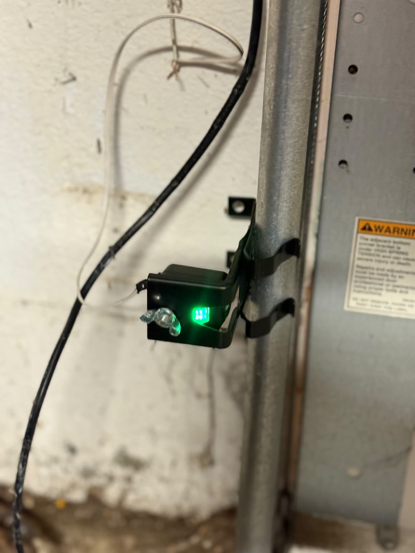 New garage door safety sensor with green indicator light, freshly installed