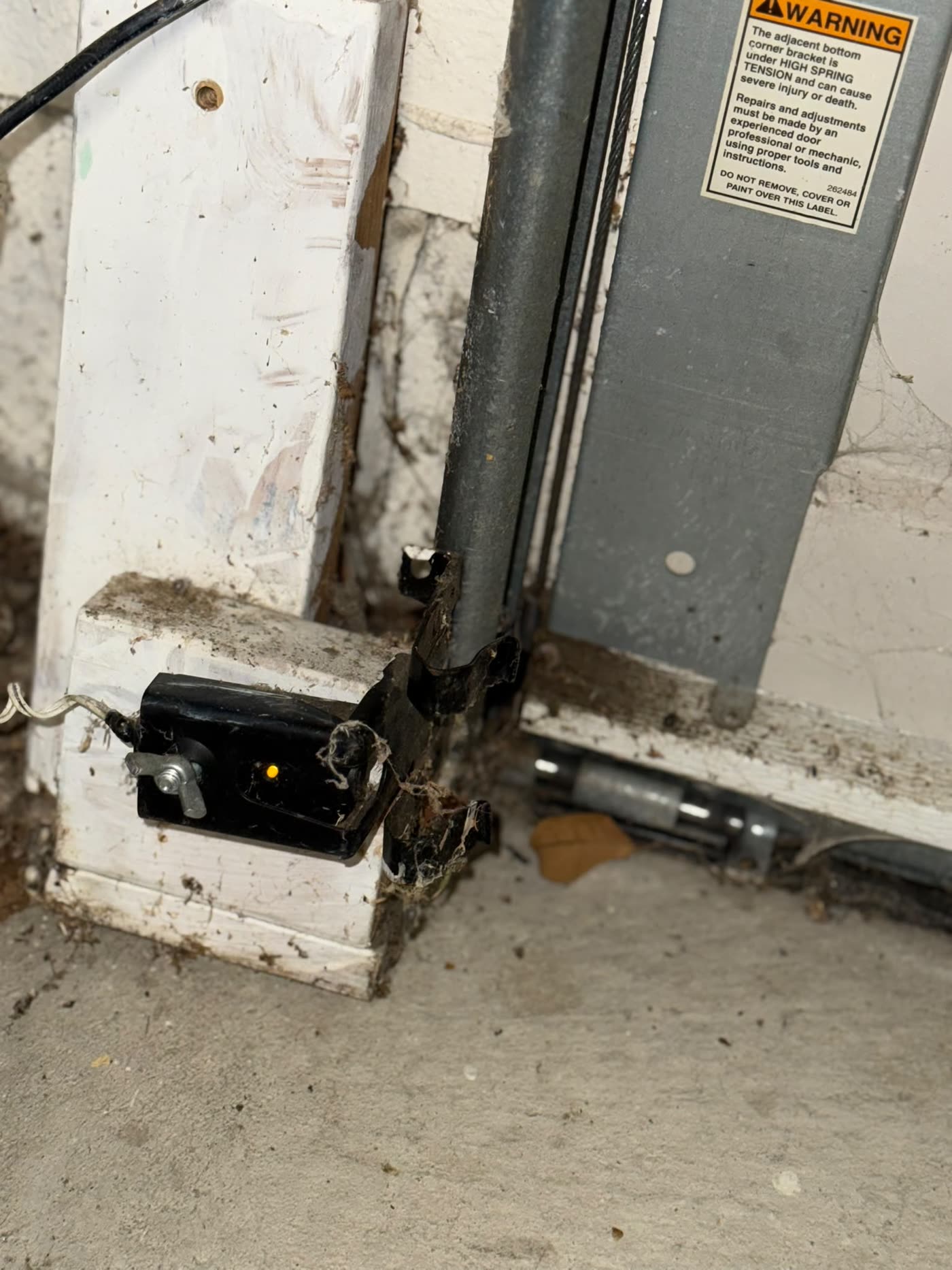 Corroded garage door safety sensor covered in cobwebs, before replacement
